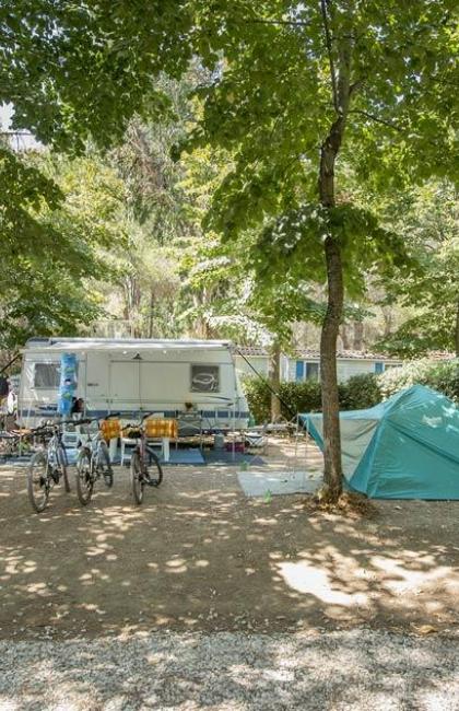 Campeggio con roulotte, tenda, amache e biciclette sotto gli alberi.