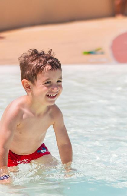 Bambino felice gioca in piscina, risate e acqua scintillante.