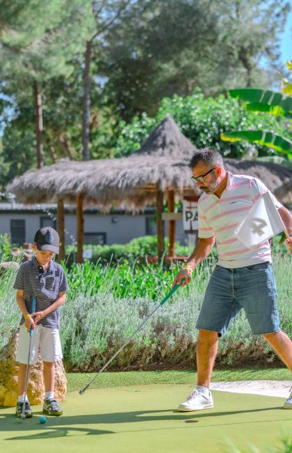 Padre e figlio giocano a mini golf in un ambiente verde e sereno.