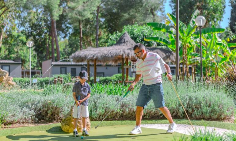 Padre e figlio giocano a mini golf in un ambiente verde e sereno.