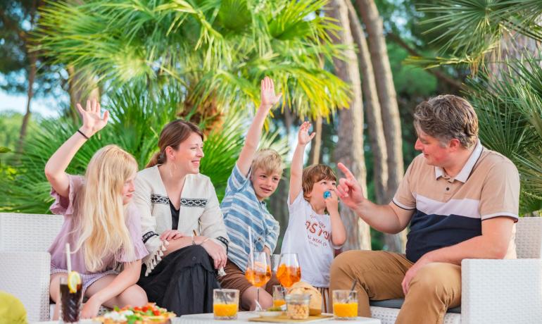 Famiglia felice all'aperto, sorrisi e mani alzate tra palme.