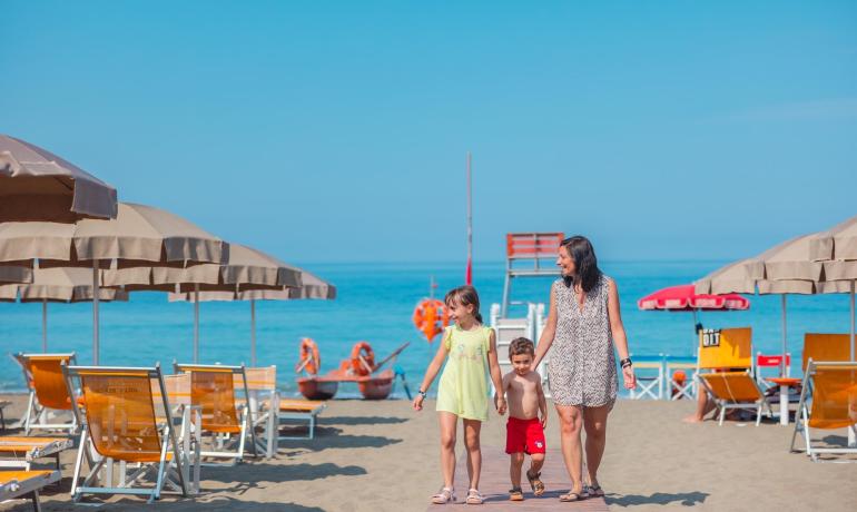 Famiglia felice cammina sulla spiaggia sotto un cielo azzurro.