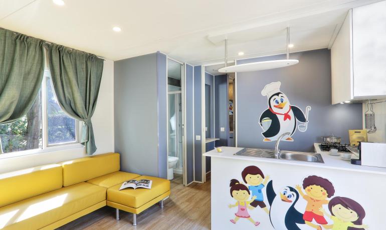 Interno luminoso e colorato con divano giallo e decorazioni di pinguini allegri.
