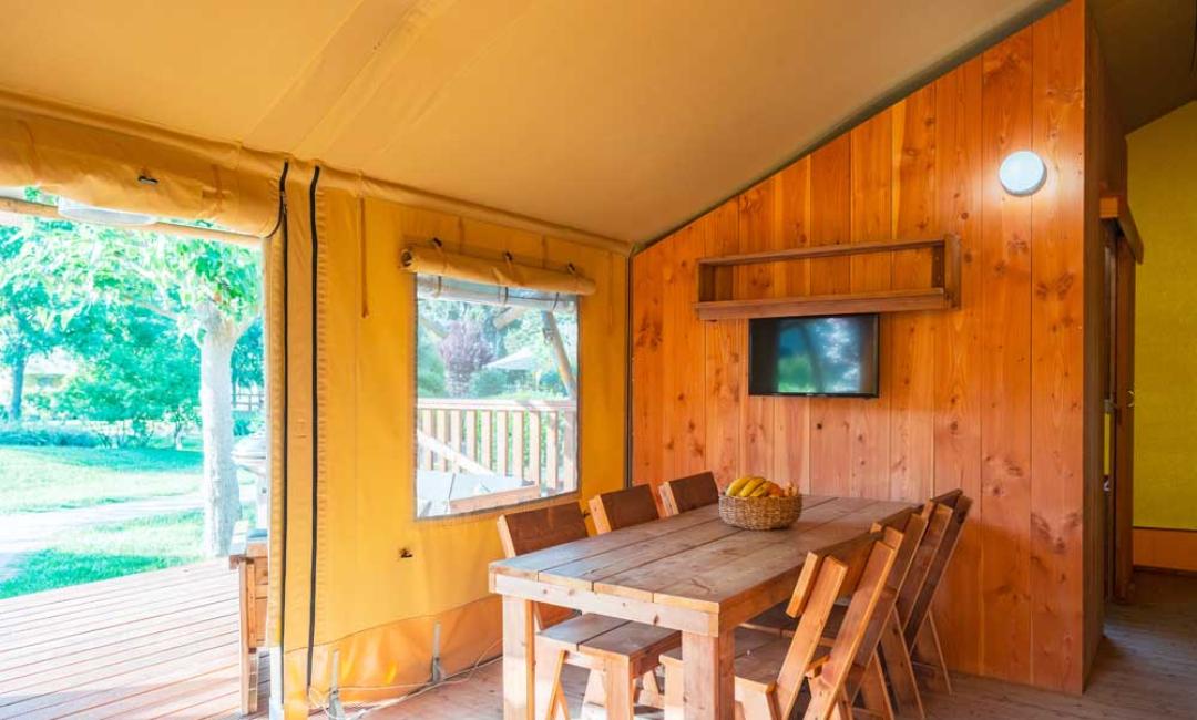 Interiør af en glamping-telt med træbord og stole.