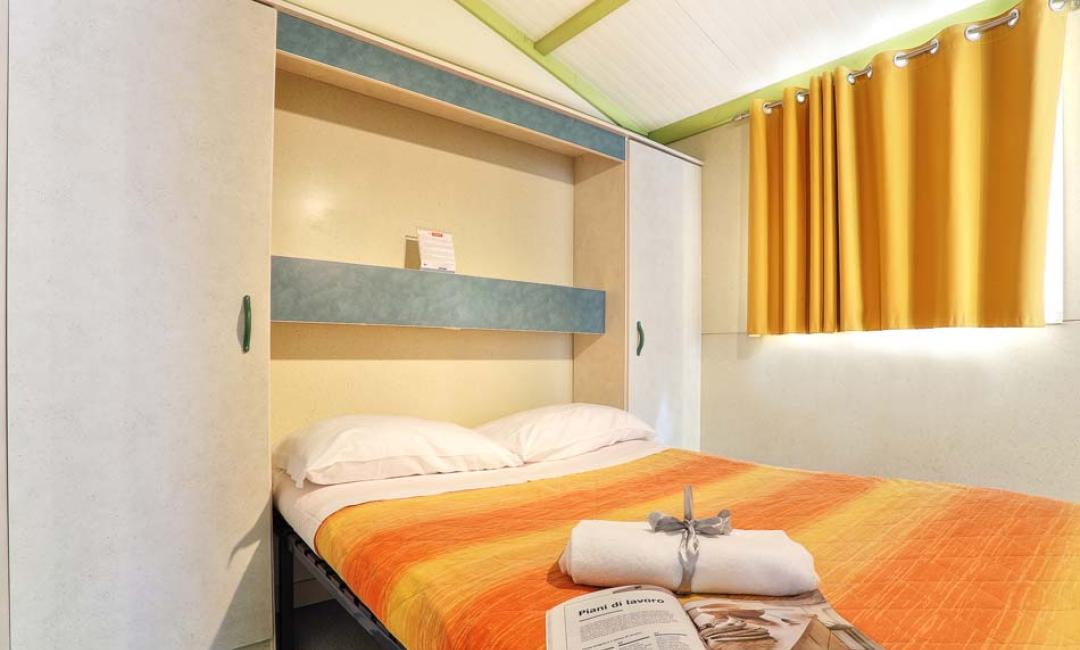 Slaapkamer met tweepersoonsbed, kast en raam met gele gordijnen.