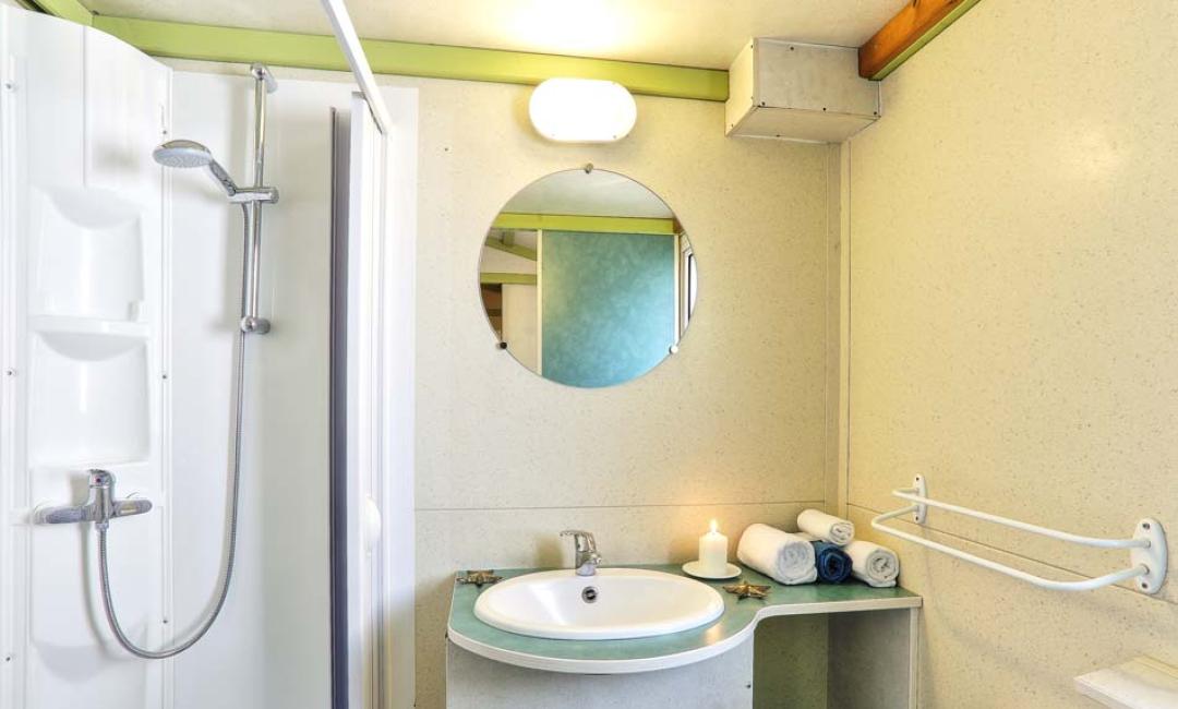 Heldere badkamer met douche, wastafel en ronde spiegel.