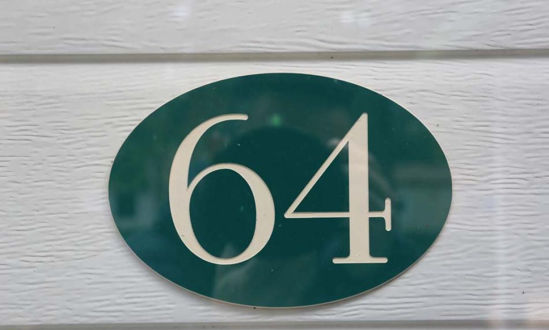Huisnummer 64 op een groene ovale achtergrond.