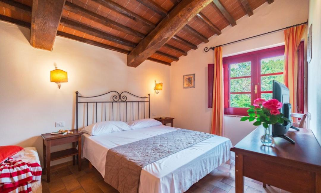 Chambre confortable avec lit double, poutres apparentes et fenêtre lumineuse.