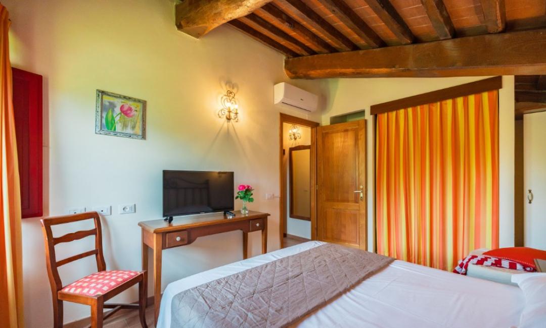 Chambre confortable avec lit, TV, chaise et décor rustique.