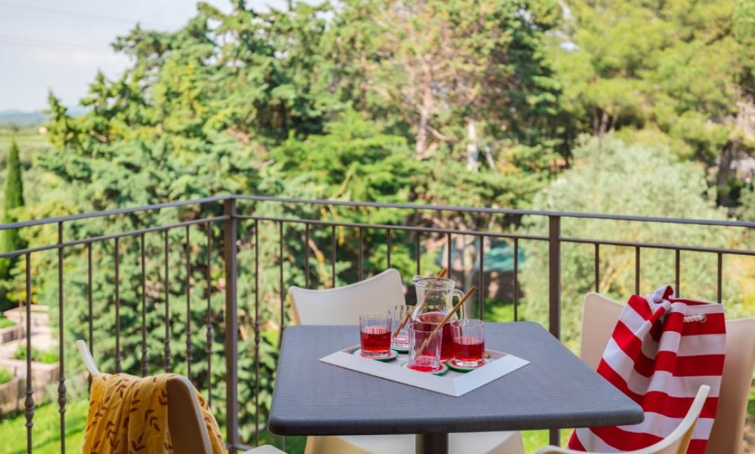 Balcon avec table, boissons rouges et vue sur des arbres verts.