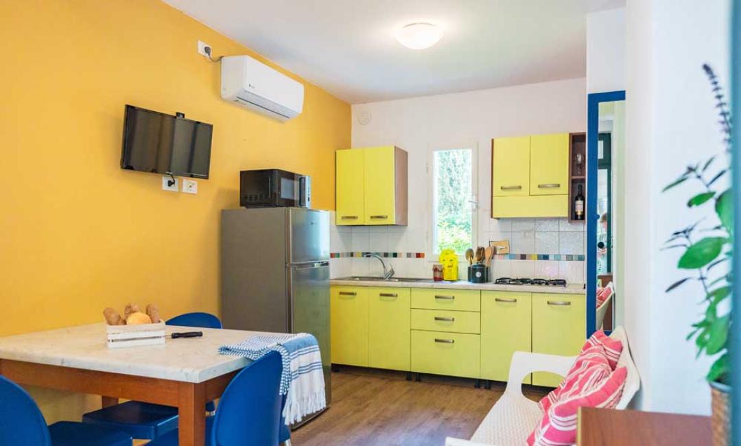 Cuisine lumineuse avec des armoires jaunes, table à manger et TV murale.