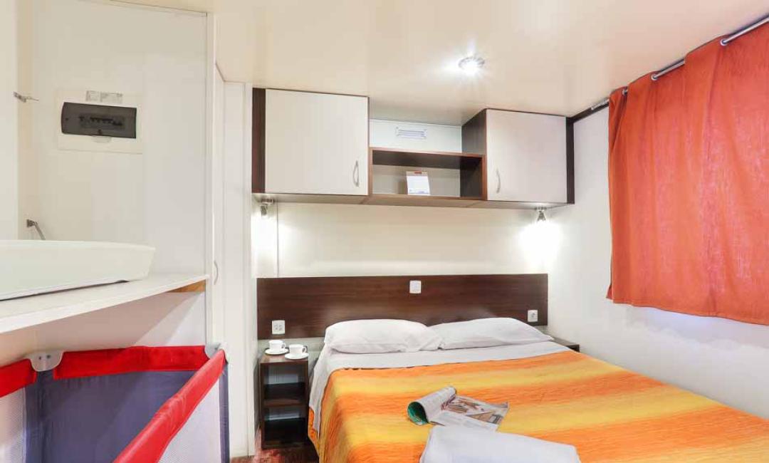 Gemütliches Zimmer mit Doppelbett, Kleiderschrank und Fenster mit orangefarbenen Vorhängen.