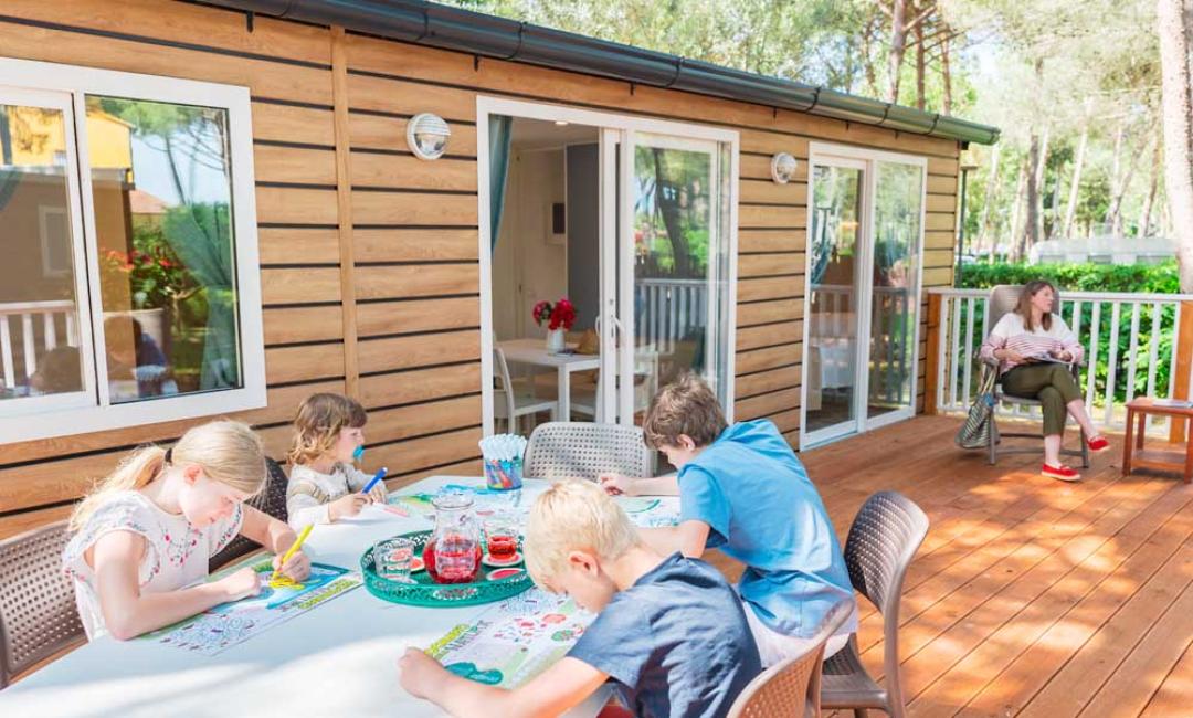 Enfants dessinant en plein air, adulte lisant en arrière-plan.