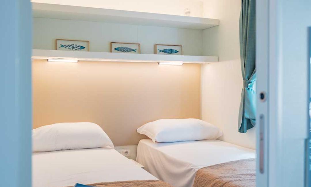 Chambre avec deux lits simples, décorations marines et fenêtre avec rideau.