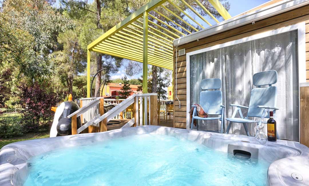 Outdoor hot tub with chairs and wine, surrounded by nature.