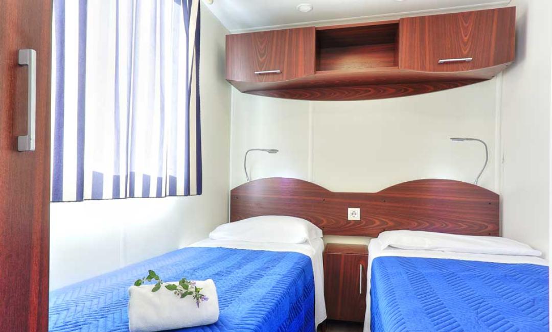 Zimmer mit zwei Einzelbetten, blauen Bettdecken und einem Holzschrank.