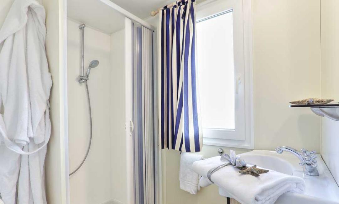 Modernes Badezimmer mit Dusche, Waschbecken und weißen Bademänteln.