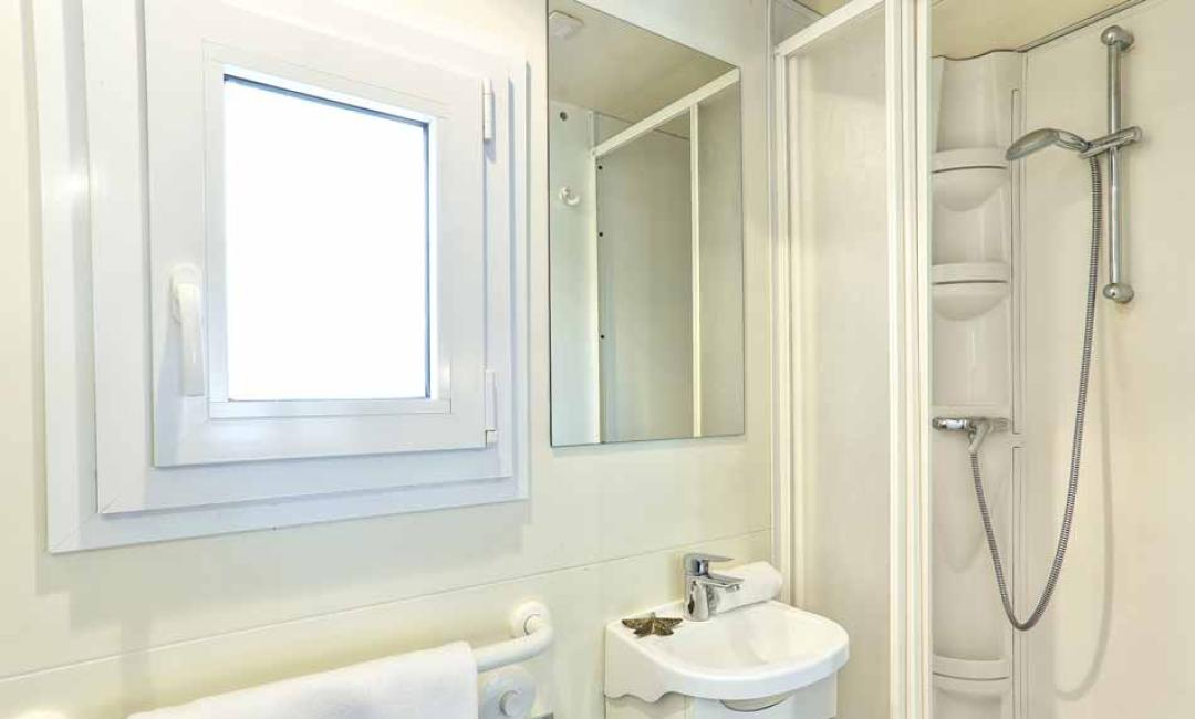 Badezimmer mit Dusche, Waschbecken, Spiegel und Fenster.