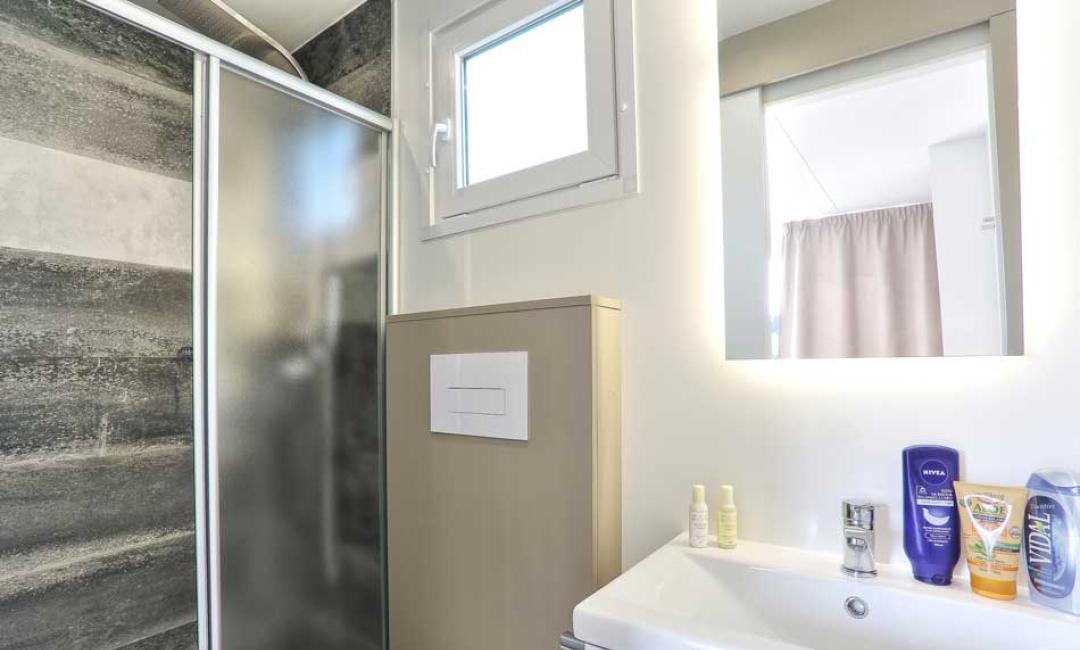 Salle de bain moderne avec douche, miroir éclairé et produits de soin.