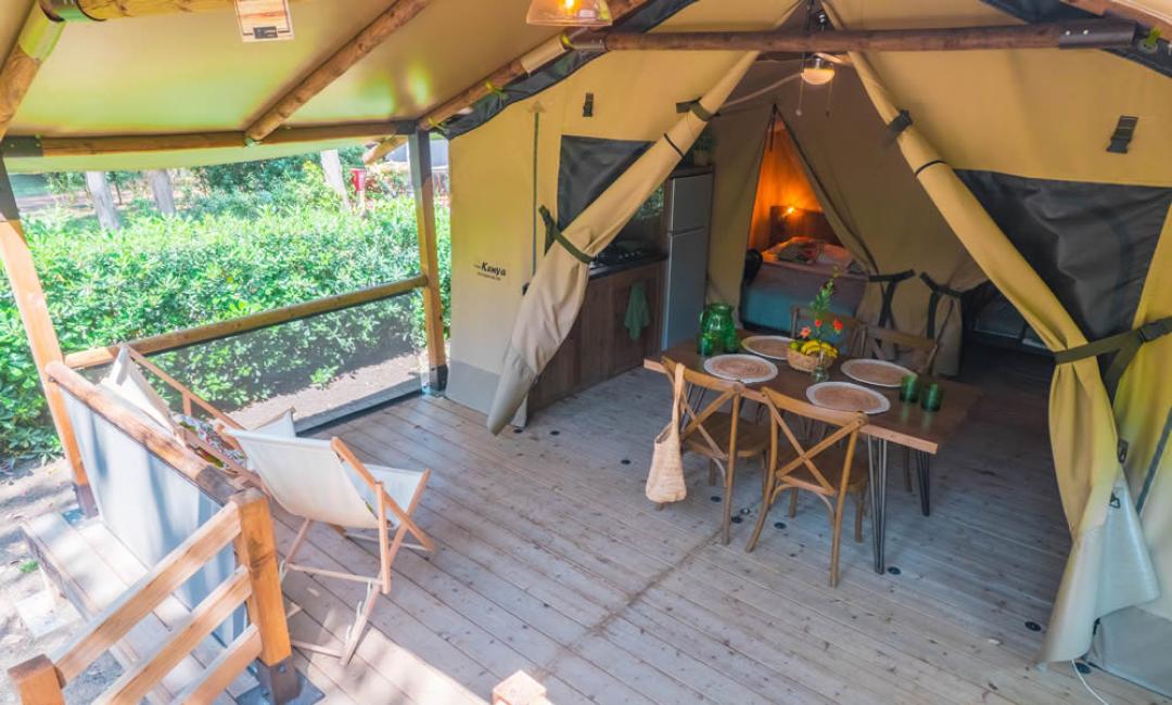 Tente glamping avec véranda, cuisine et coin nuit entourée de nature.