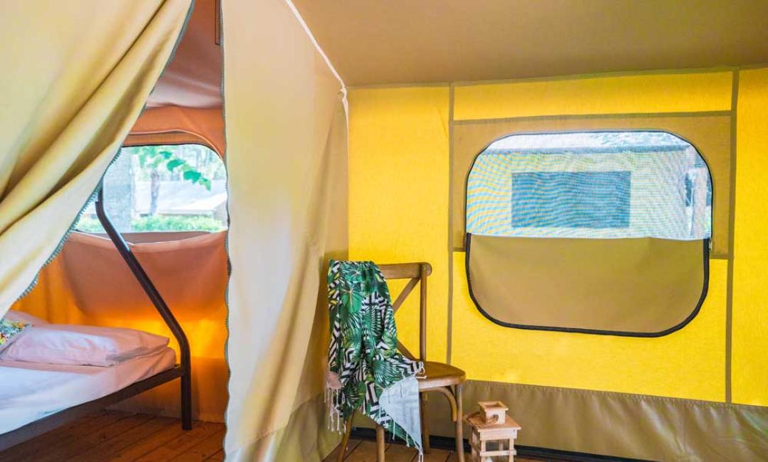 Intérieur d'une tente glamping avec lit, chaise et décorations.