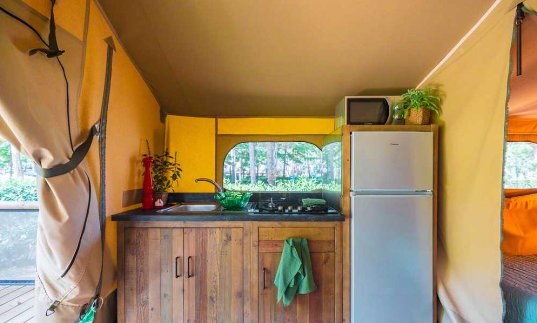 Cuisine sous tente avec réfrigérateur, évier et plantes.