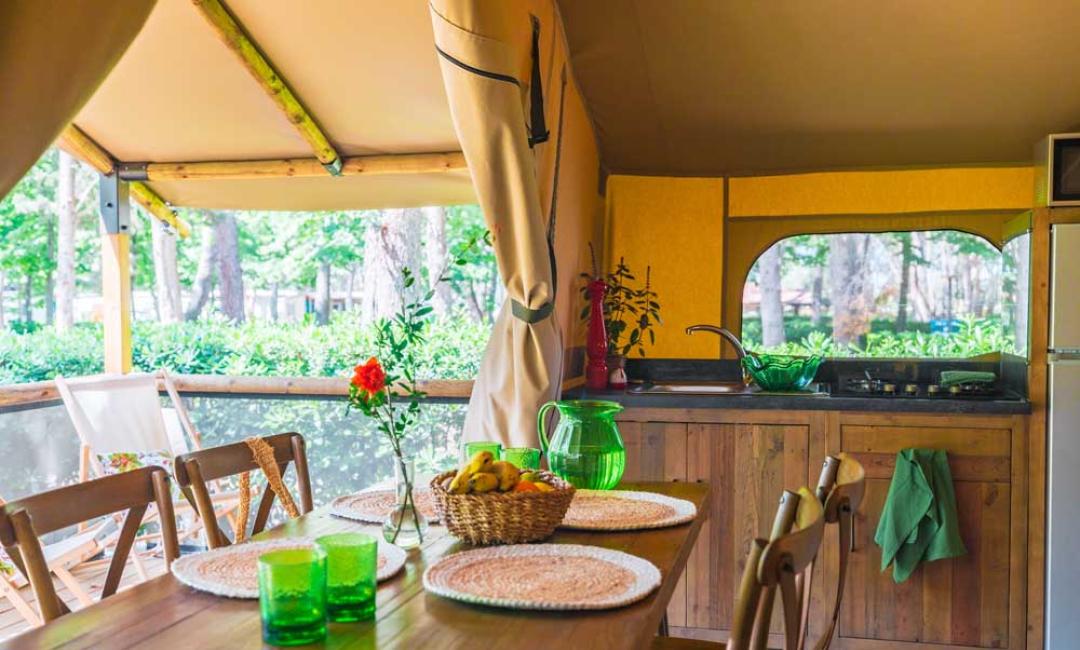 Tente glamping avec cuisine, table et vue sur la forêt.