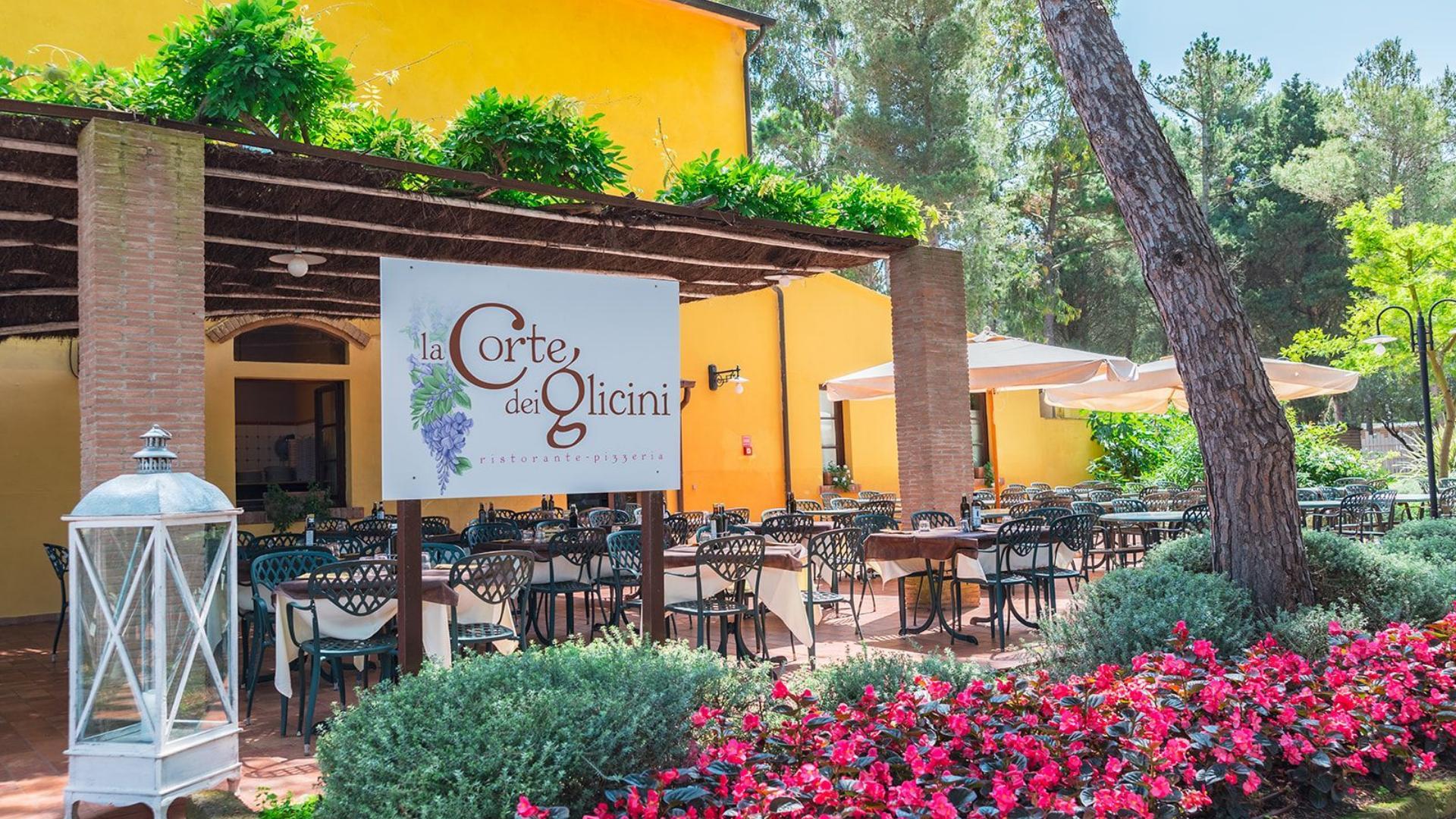 Restaurant and pizzeria with outdoor terrace, surrounded by flowers and trees.
