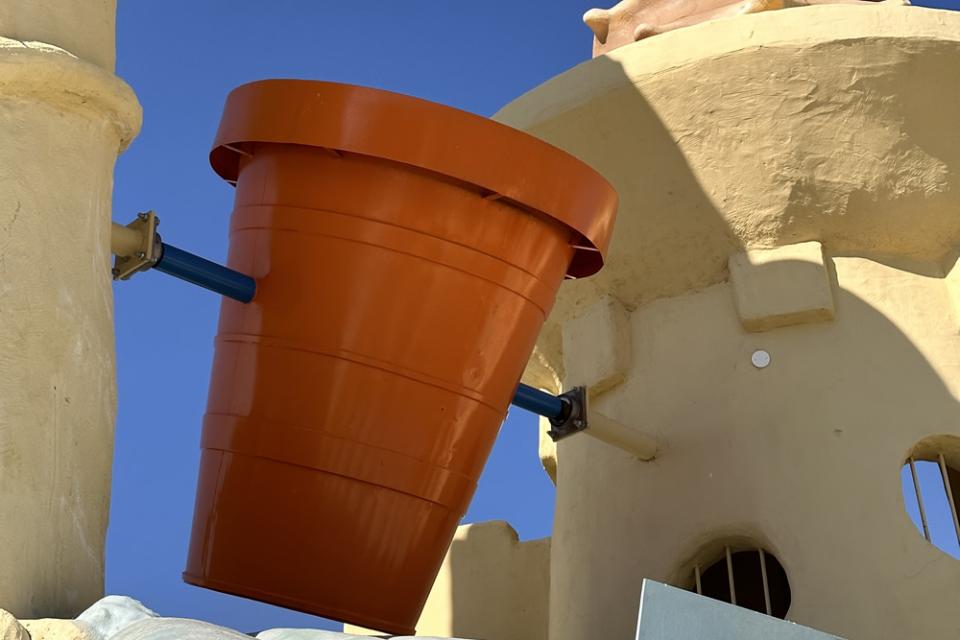 Grande vaso arancione su struttura gialla con cielo blu.