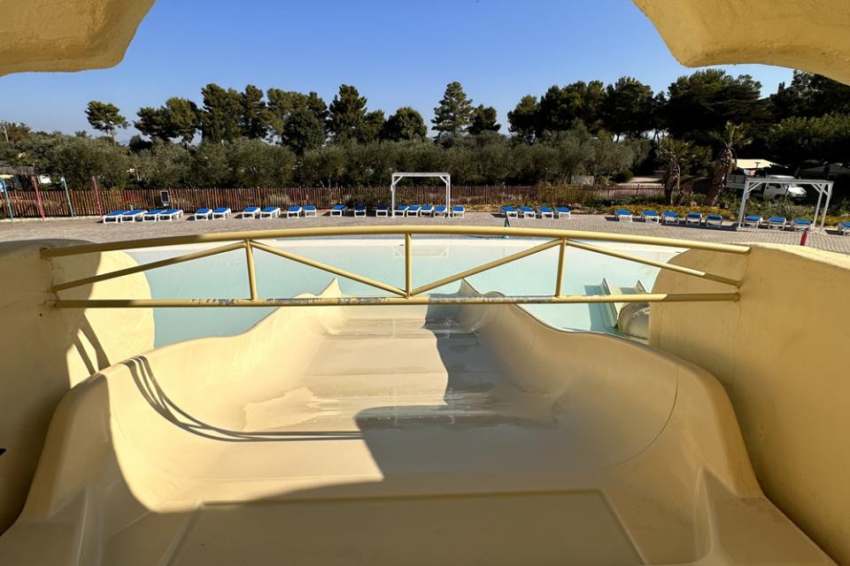 Scivolo acquatico vuoto con piscina e lettini sullo sfondo.
