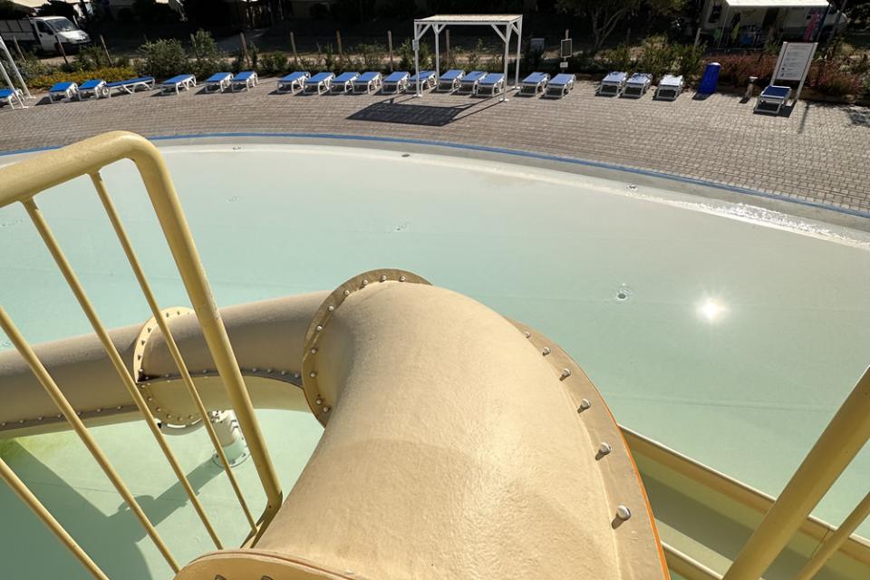 Scivolo d'acqua che si affaccia su una piscina vuota con lettini.